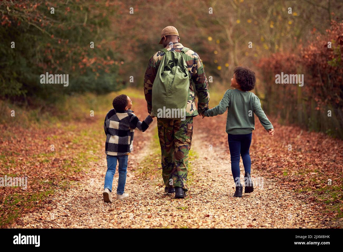 Vista posteriore del soldato americano in uniforme che ritorna a casa alla famiglia tenendo le mani con due bambini Foto Stock