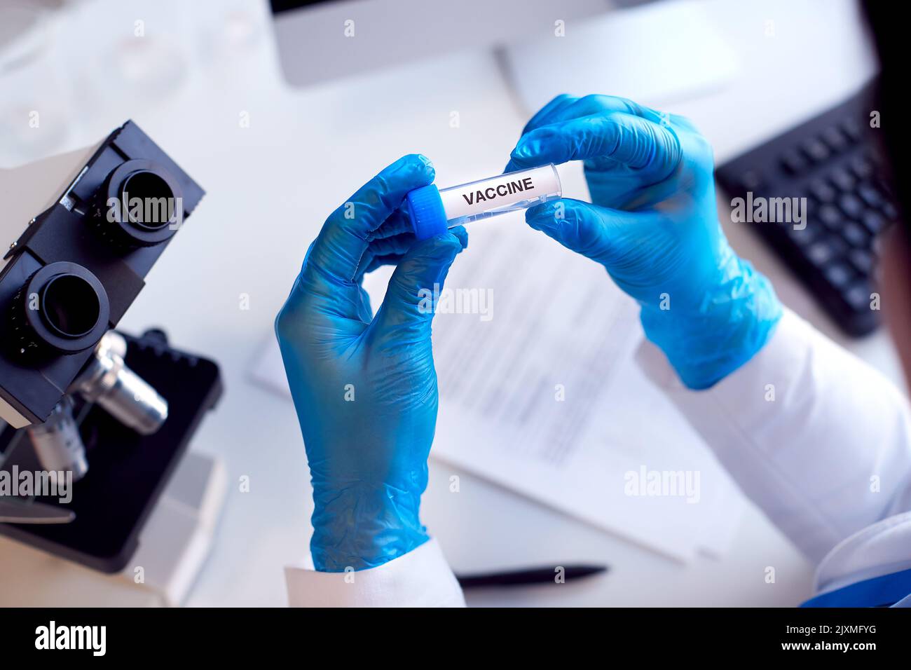 Primo piano del lavoratore di laboratorio che conduce ricerche utilizzando la provetta per test con microscopio vaccino etichettato Foto Stock