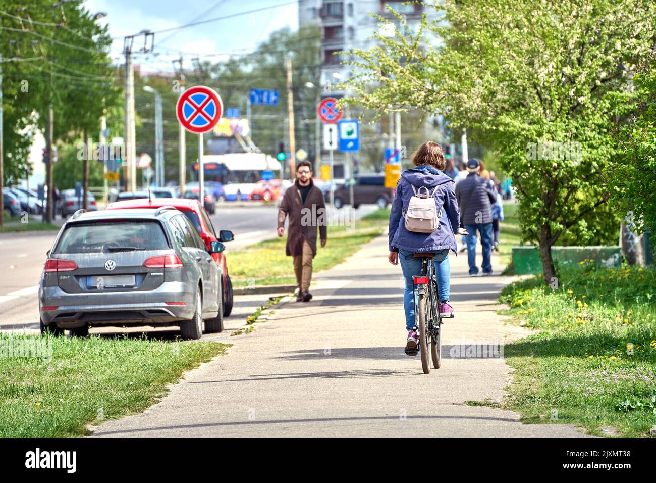 RIGA, LETTONIA - 13 MAGGIO 2022: Donna in bicicletta su un marciapiede. Un uomo in un cappotto e occhiali da sole cammina nella direzione opposta durante la giornata di sole. Foto Stock