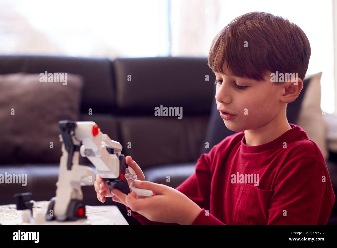Ragazzo che indossa i pigiami che costruano il braccio robotico del kit di plastica a casa Foto Stock