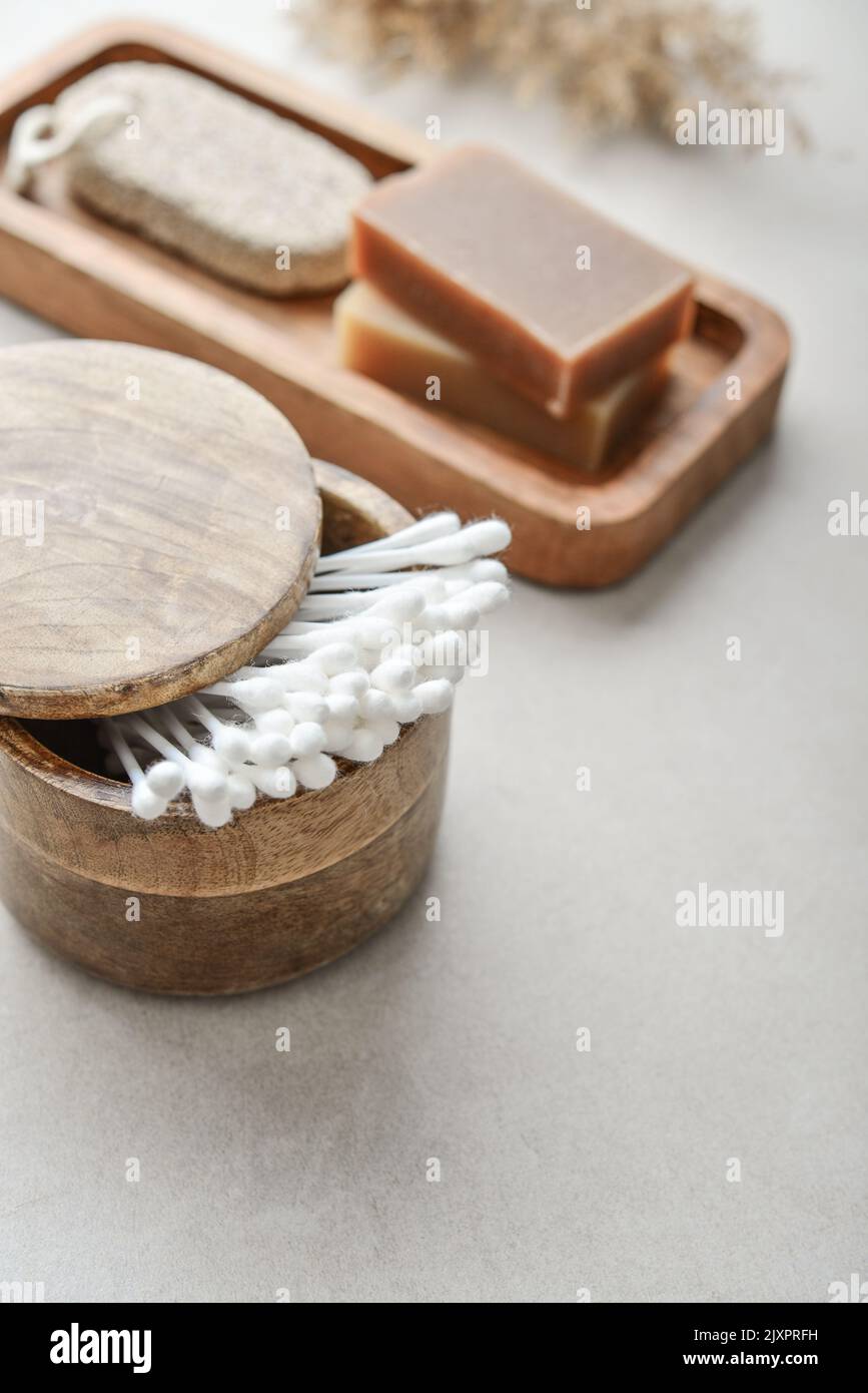 Сotton boccioli in scatola di legno con sapone e pietra pomice su vassoio di legno su fondo di cemento chiaro Foto Stock