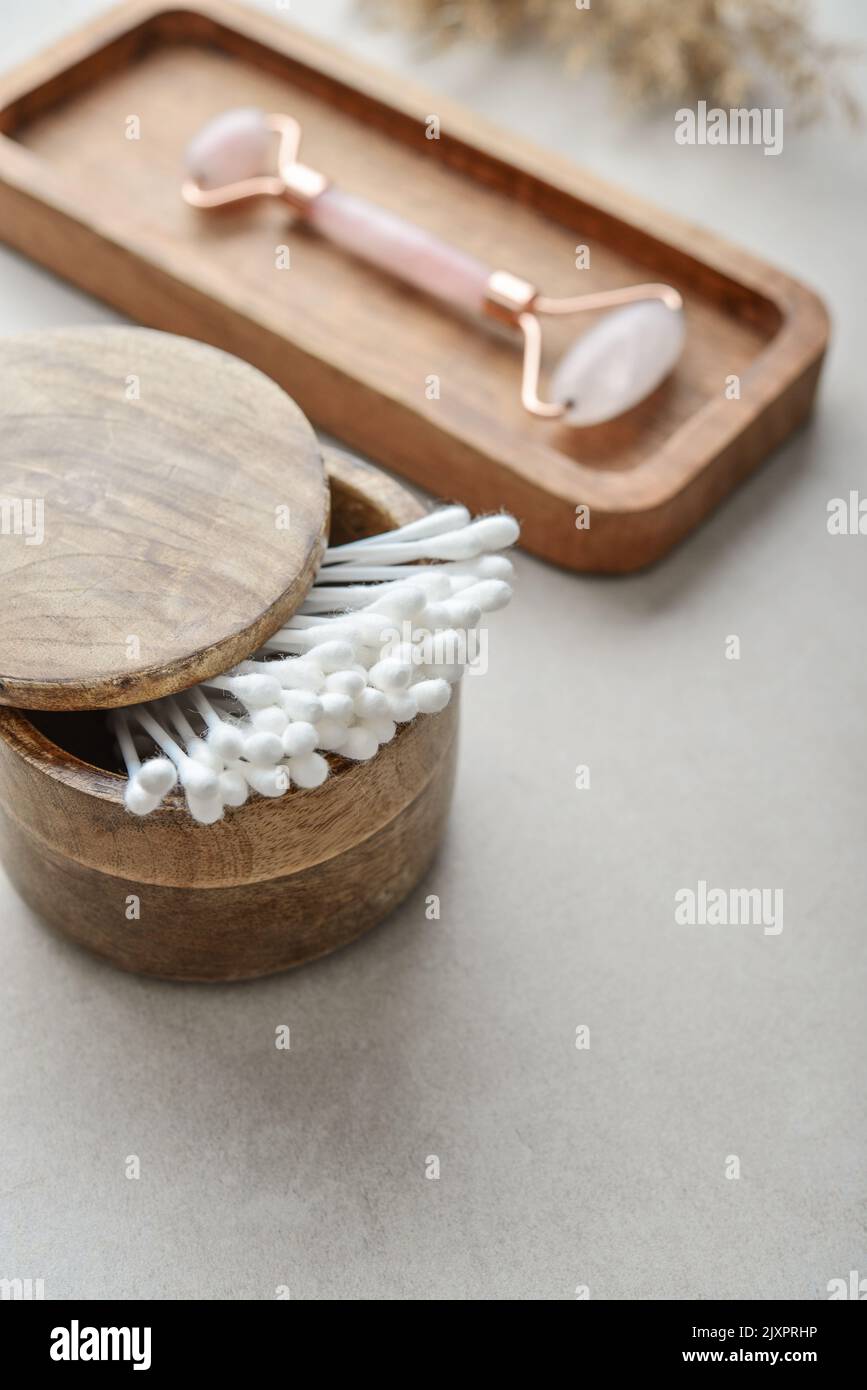 Сotton boccioli in scatola di legno con rullo facciale in quarzo rosa su vassoio di legno su fondo in cemento chiaro Foto Stock
