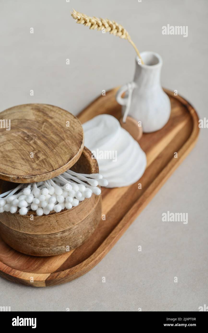 Сotton boccioli in scatola di legno con tamponi tondi in cotone facciale su vassoio di legno su fondo di cemento chiaro Foto Stock