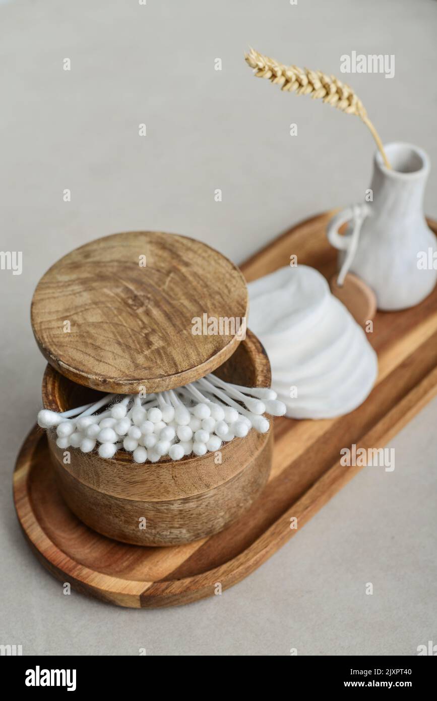 Сotton boccioli in scatola di legno con tamponi tondi in cotone facciale su vassoio di legno su fondo di cemento chiaro Foto Stock