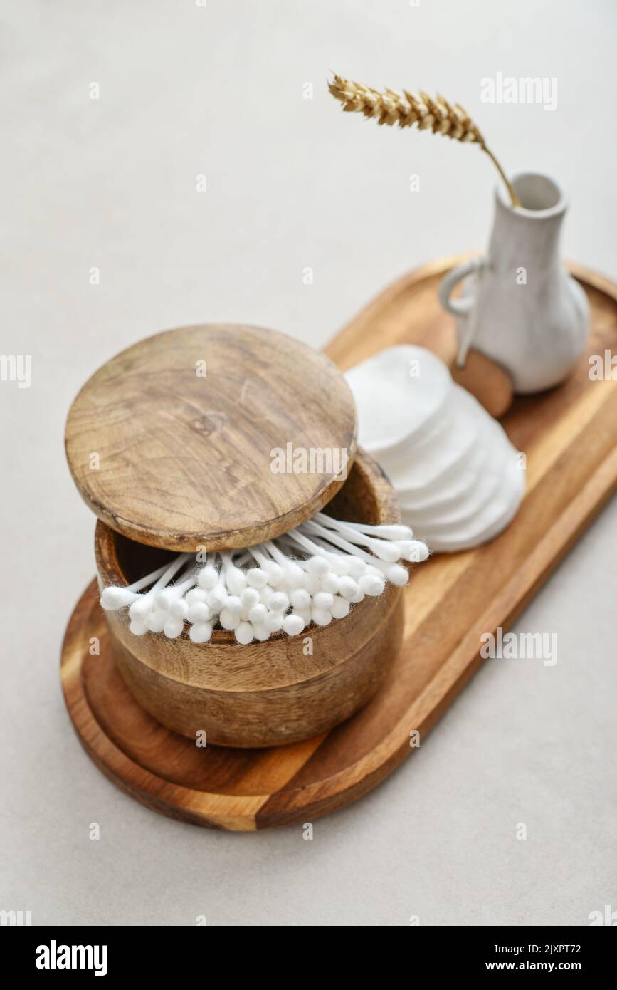 Сotton boccioli in scatola di legno con tamponi tondi in cotone facciale su vassoio di legno su fondo di cemento chiaro Foto Stock