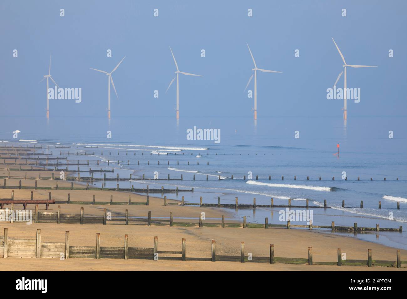 Groynes sulla spiaggia di Redcar con turbine eoliche in lontananza. Foto Stock