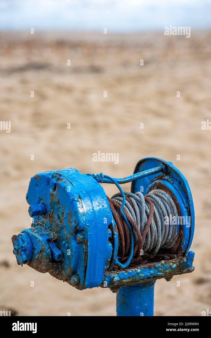 vecchio verricello meccanico blu per tirare barche da pesca sulla spiaggia a swanage in dorset, verricello vintage dipinto di blu con filo arrugginito sulla spiaggia. Foto Stock