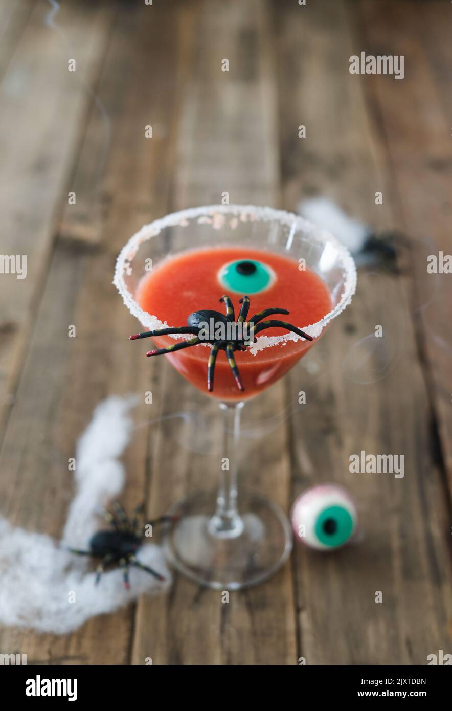 Terrificante cocktail rosso con ragno su sfondo di legno per Halloween con decorazione. Foto verticale. Spazio di copia. Foto Stock