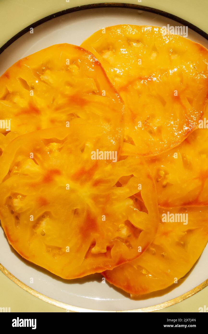 succosa pomodoro giallo a fette su piatto giallo pallido, oro, bianco Foto Stock