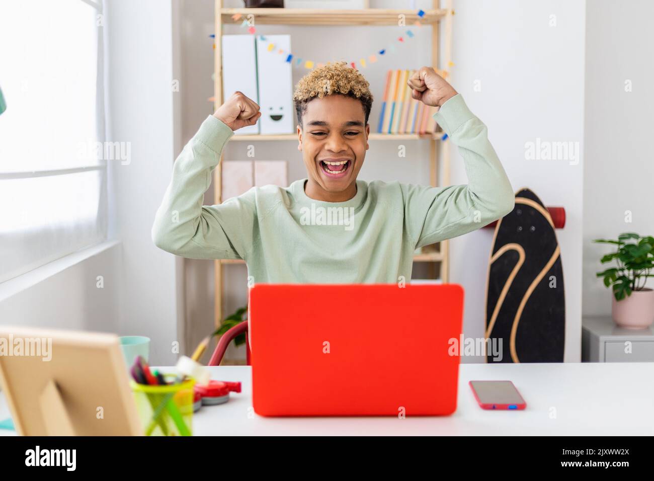 Giovane latino ispanico eccitato che celebra le buone notizie usando il laptop a casa Foto Stock