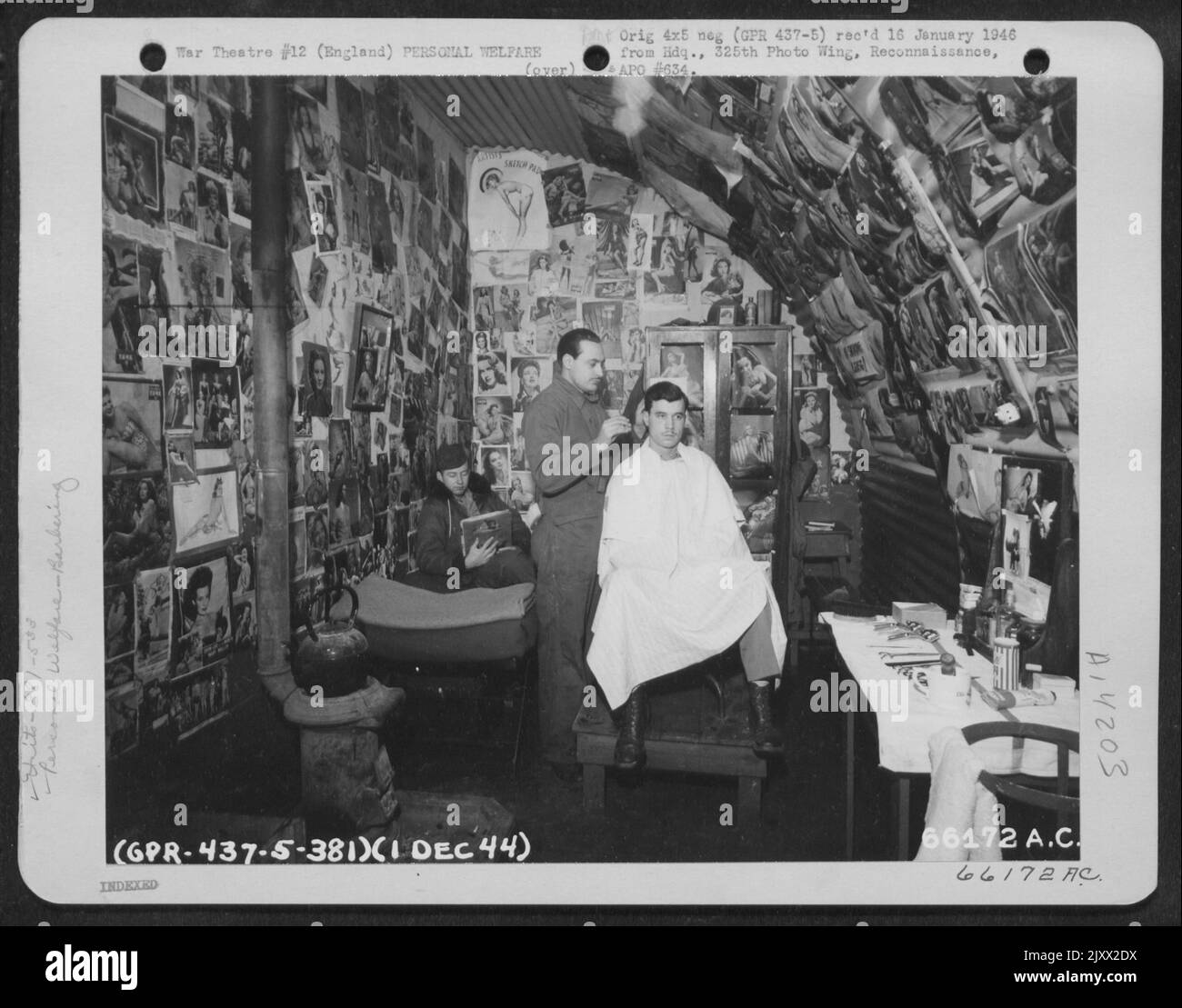 Una moltitudine di immagini puntellate che adornano la parete del Barbiere dello Squadrone della bomba del 533Rd cattura l'occhio del cliente mentre il Barbiere gli dà Un rivestimento. 381st Bomb Group, Inghilterra, 1 dicembre 1944. Foto Stock