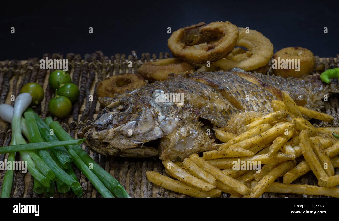 Trota fritta, patatine fritte, anelli di cipolla, calamansi, cipolle verdi e pepe su piatto di bambù. Foto Stock