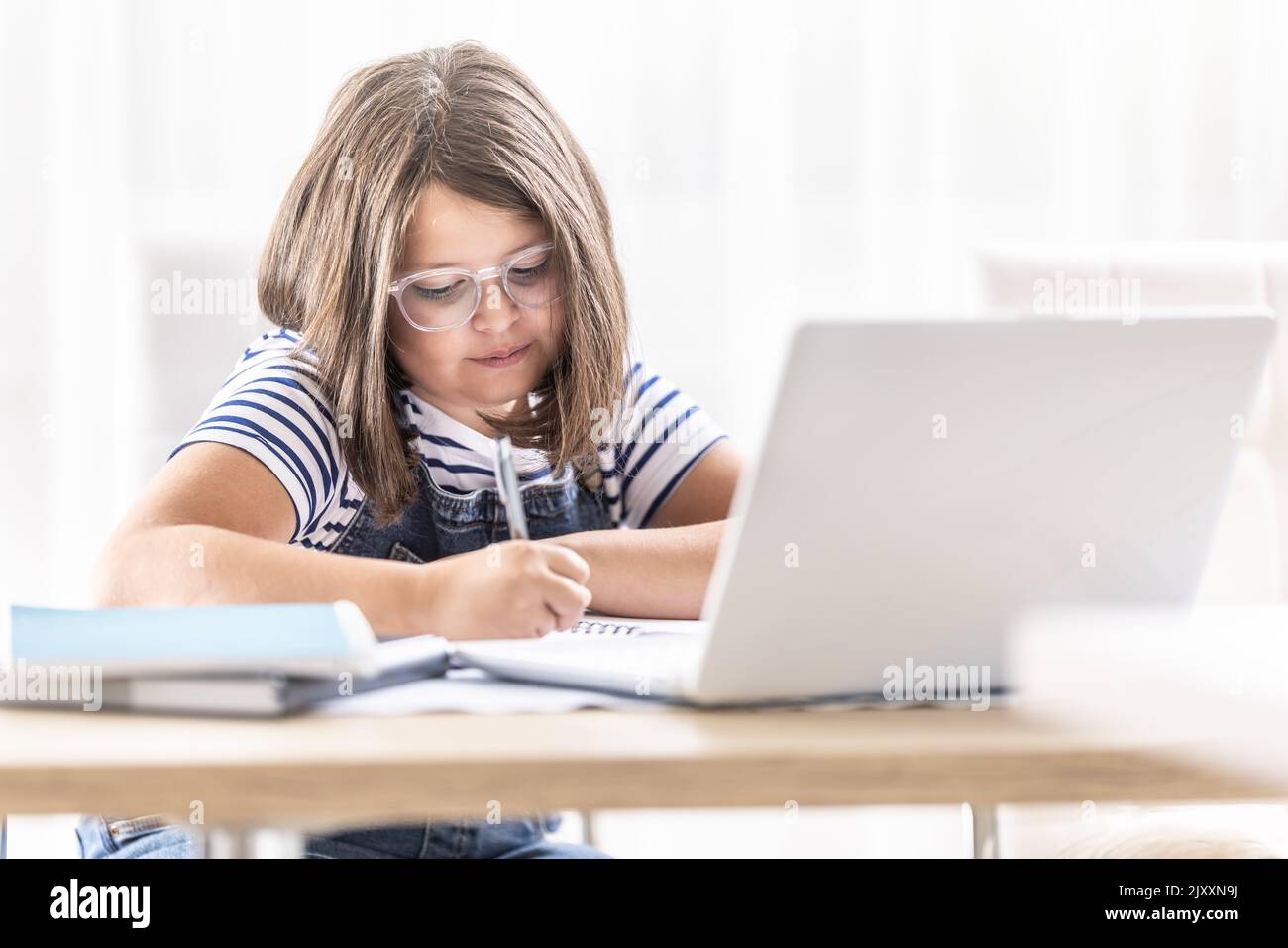 La ragazza in vetri scrive giù le note che studiano via l'apprendimento distante sopra il Internet. Foto Stock