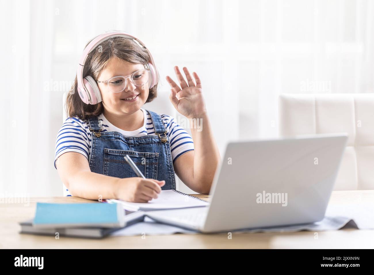 Chubby studentessa in occhiali e cuffie ondeggia ai suoi compagni di scuola sul computer durante studi a distanza. Foto Stock