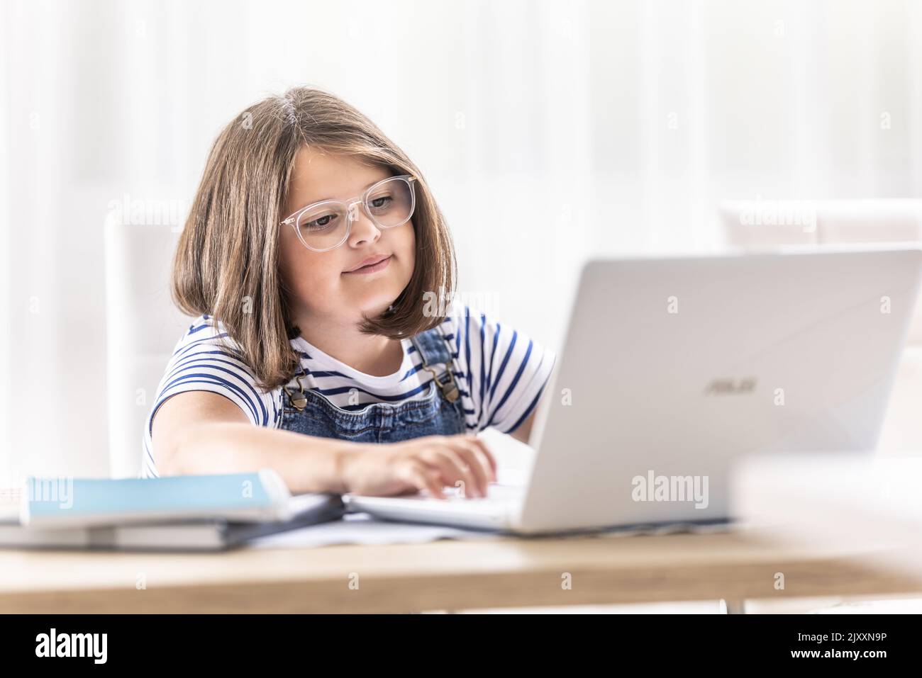 Una ragazza con la faccia rotonda che indossa gli occhiali si trova dietro un notebook che lo guarda dentro. Foto Stock
