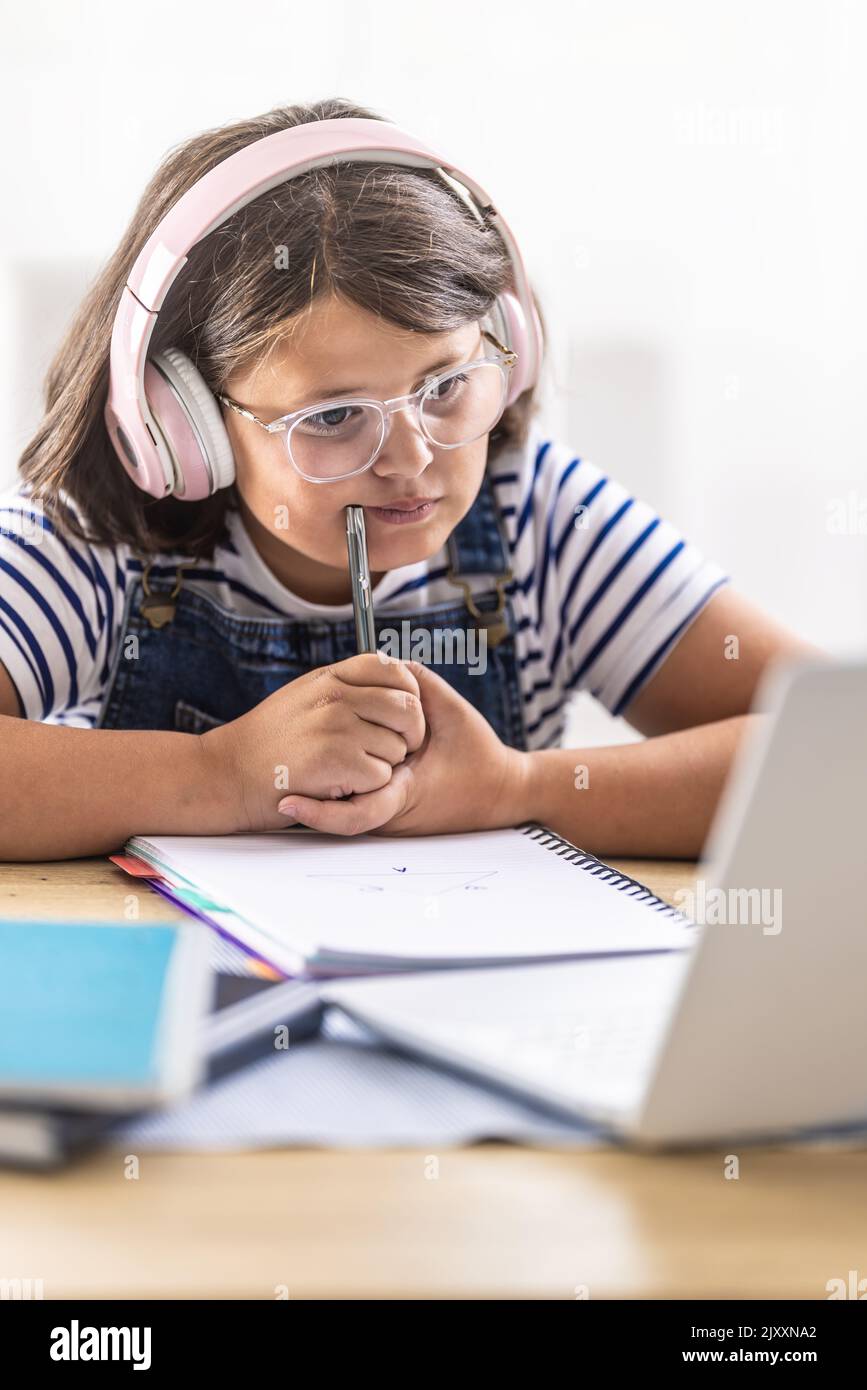 Ragazza che studia duro in occhiali indossa cuffie e masticare sulla matita in mano guardando il pc. Foto Stock
