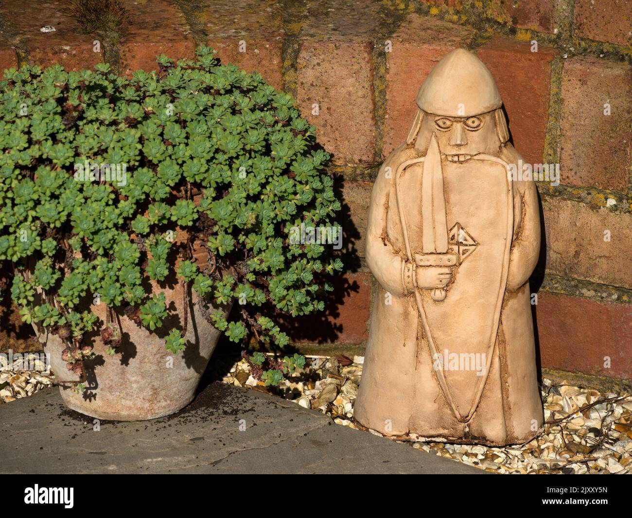 Ornamento da giardino 'Beserker' Lewis Chessman accanto alla pianta in vaso e alla parete da giardino in mattoni rossi, Regno Unito Foto Stock