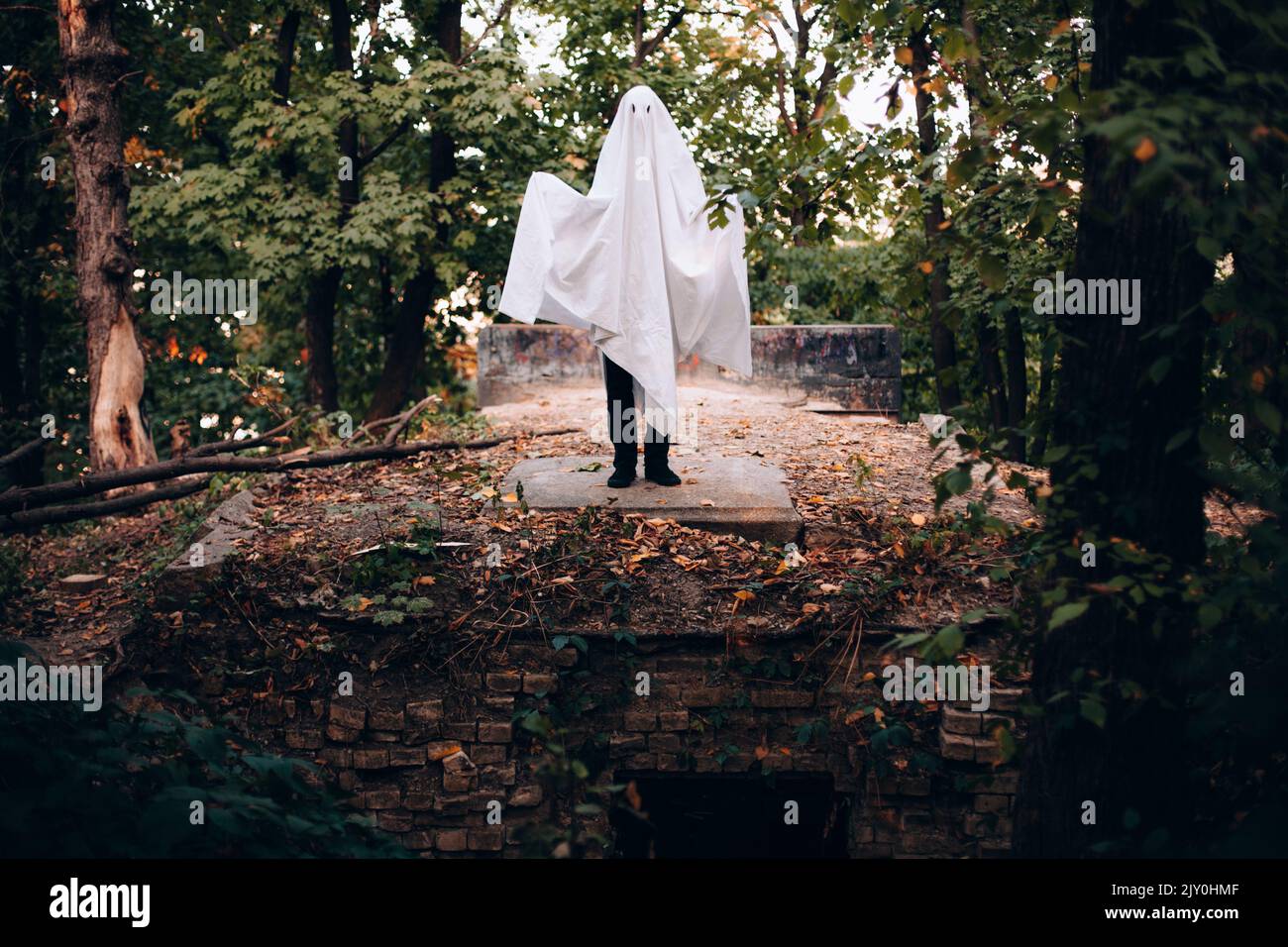 Uomo che indossa costume fantasma mentre si trova sulla tomba nel cimitero durante Halloween Foto Stock