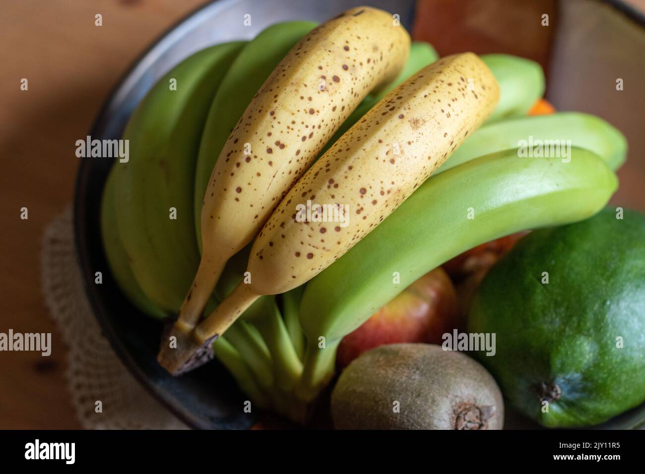 Banane macchiate di colore giallo maturo accanto alle banane verdi in un recipiente per la frutta per favorire la maturazione Foto Stock