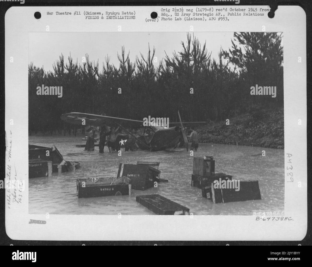 Uomini spingere Un Vultee L-5 relitto del 163rd Liaison Squadron a terra più alta per poter Salvage parti utilizzabili dell'aereo. Tre giorni di Heavy Rain trasformarono il piccolo ruscello che corre attraverso l'area in un lago. Okinawa, Ryukyu Rett. 1945. Foto Stock