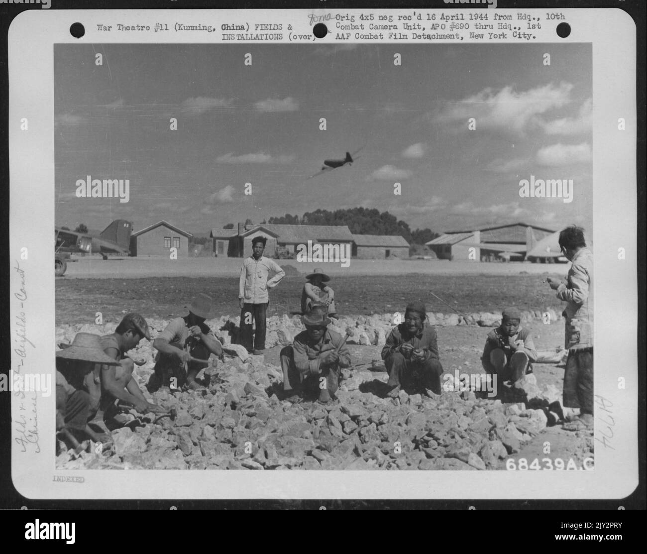 Apparentemente ignaro del Cargo aereo che circling sopra, Coolies continua a rompere roccia schiacciata che forma la fondazione di piste e strisce Taxi a Kunming, Cina. 1943. Foto Stock