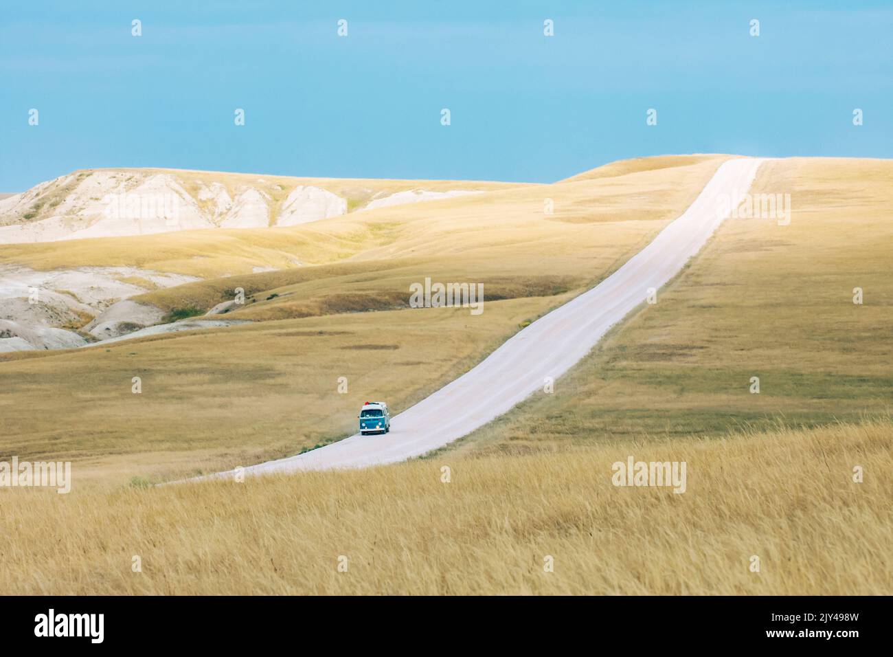 Il classico pulmino blu guida lungo la strada sterrata attraverso il paesaggio delle praterie delle grandi pianure durante il viaggio estivo su strada Foto Stock