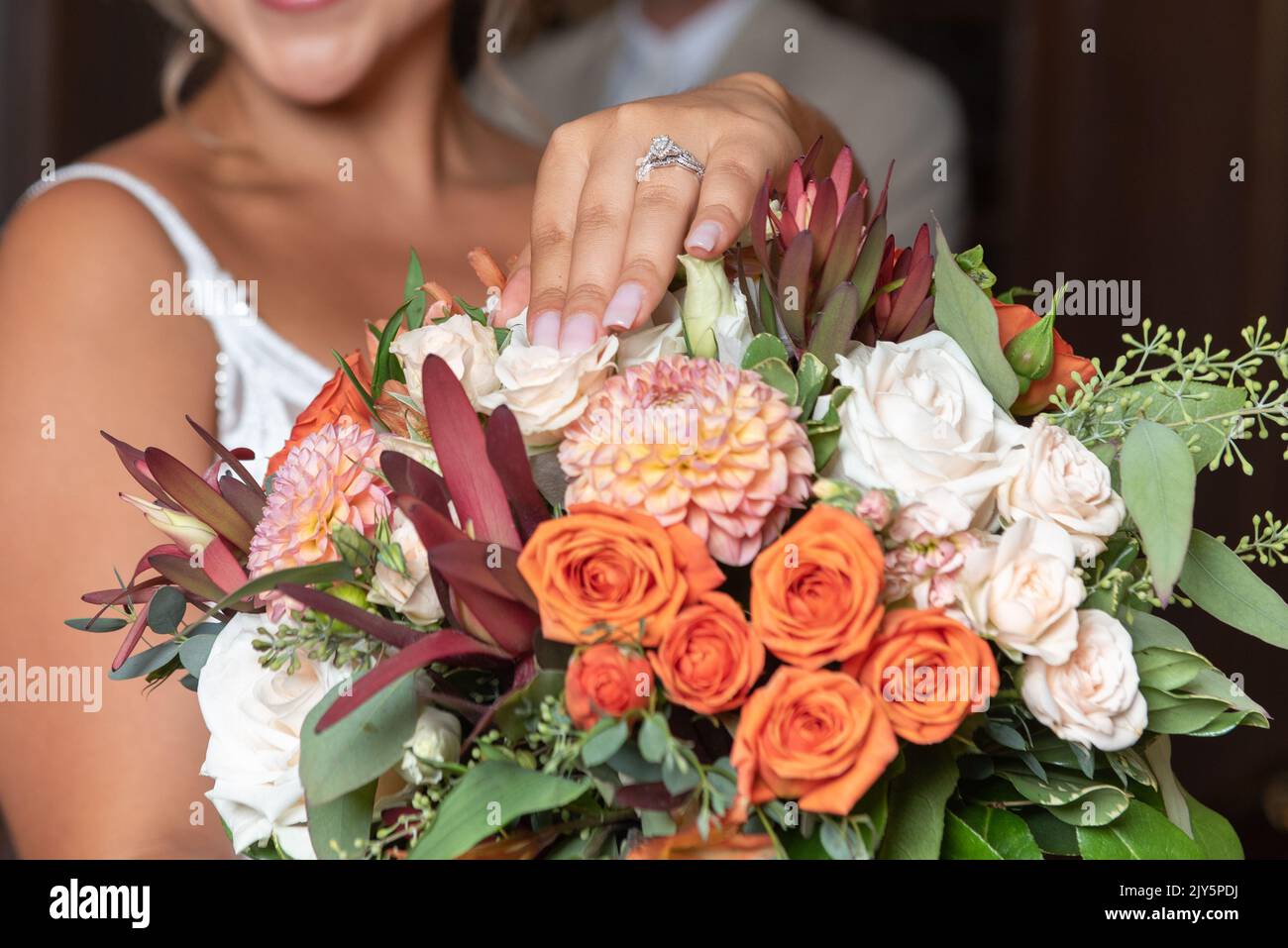 Bel diamante sull'anello di nozze della sposa che tiene il bouquet di fiori davanti allo sposo. Foto Stock