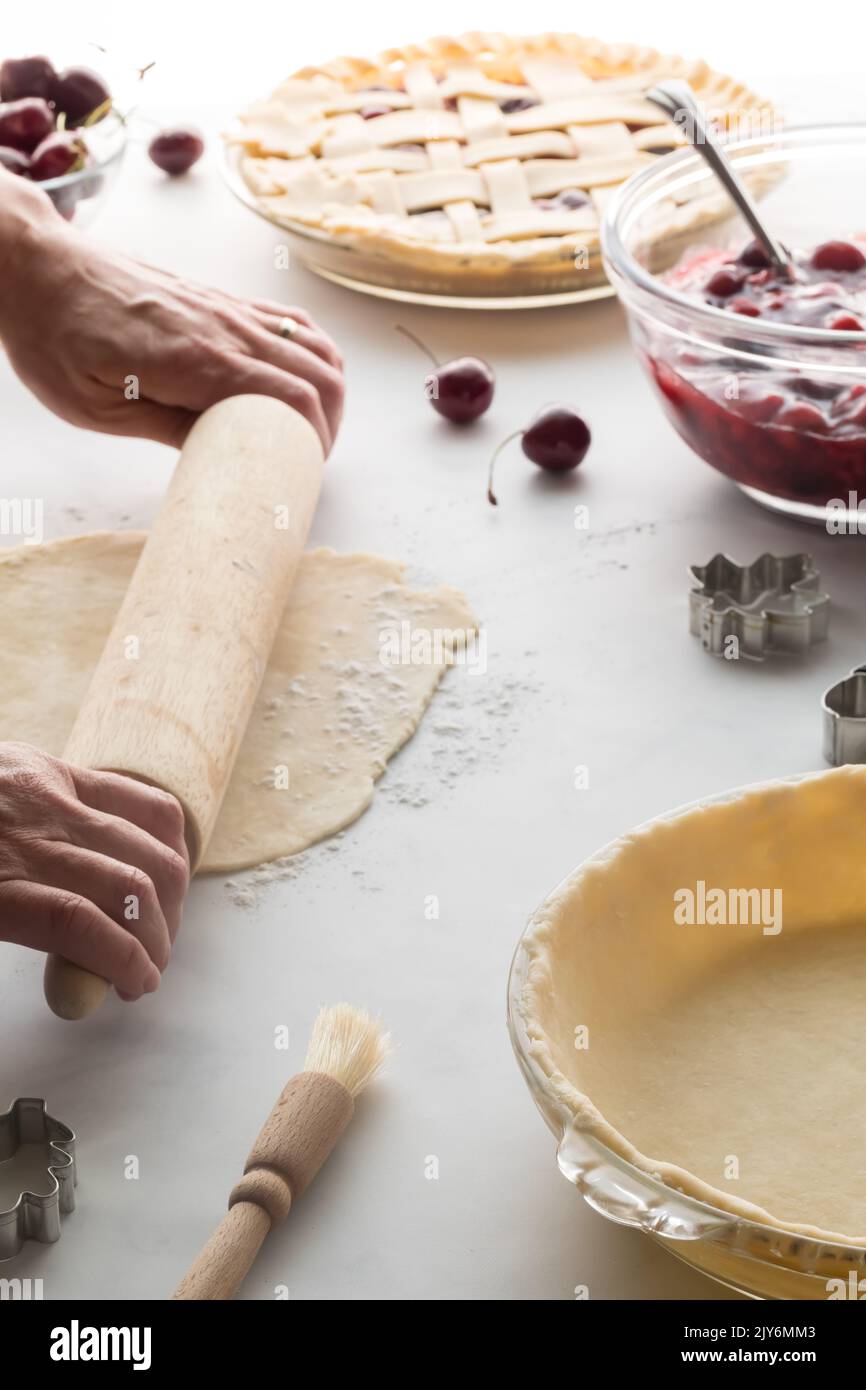 Mani che stendono l'impasto in preparazione di fare una torta di ciliegie fresca. Foto Stock