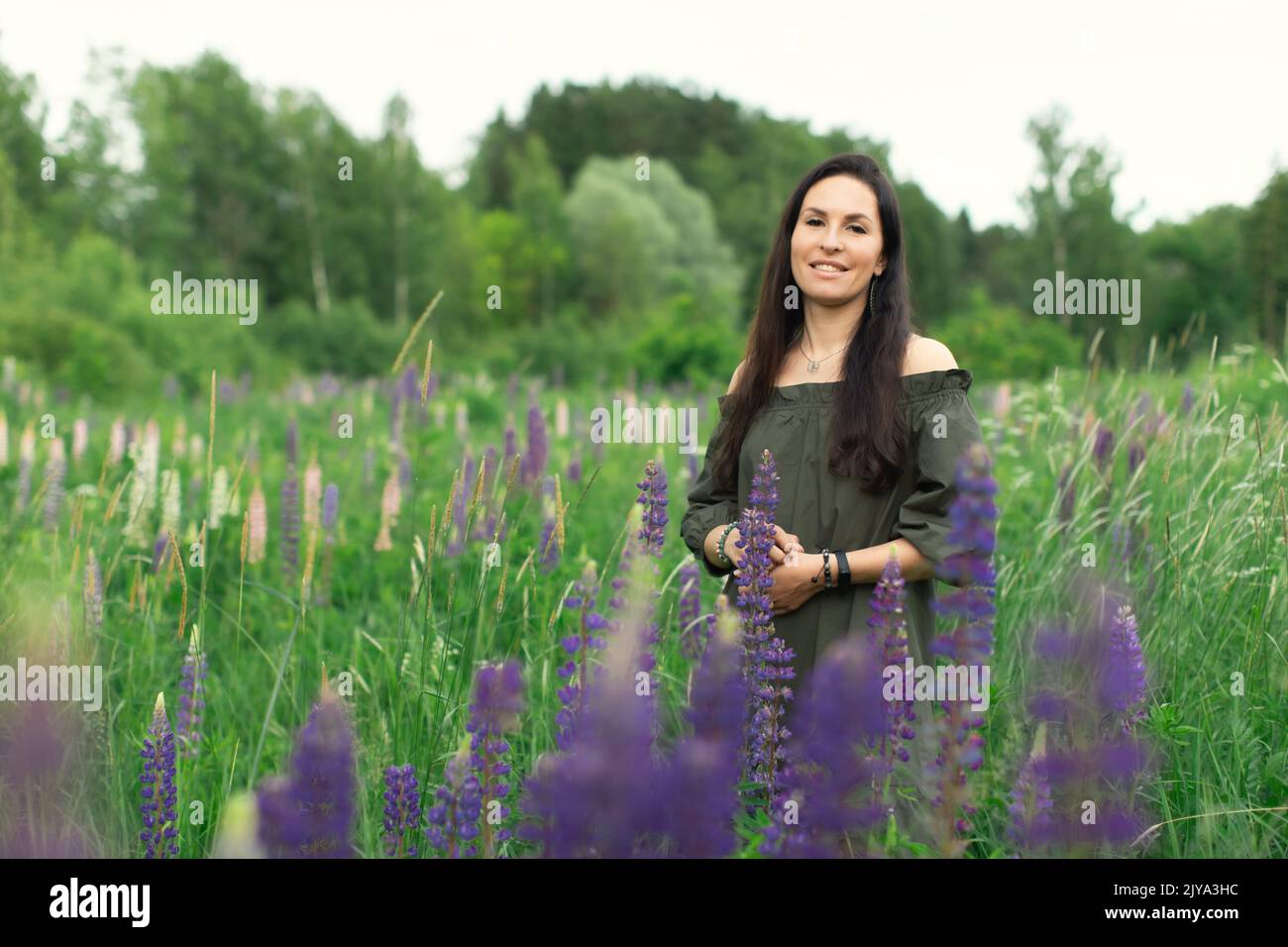Una donna attraente in un campo con un bouquet estivo di fiori selvatici Lupinus. Vista frontale. Foto Stock