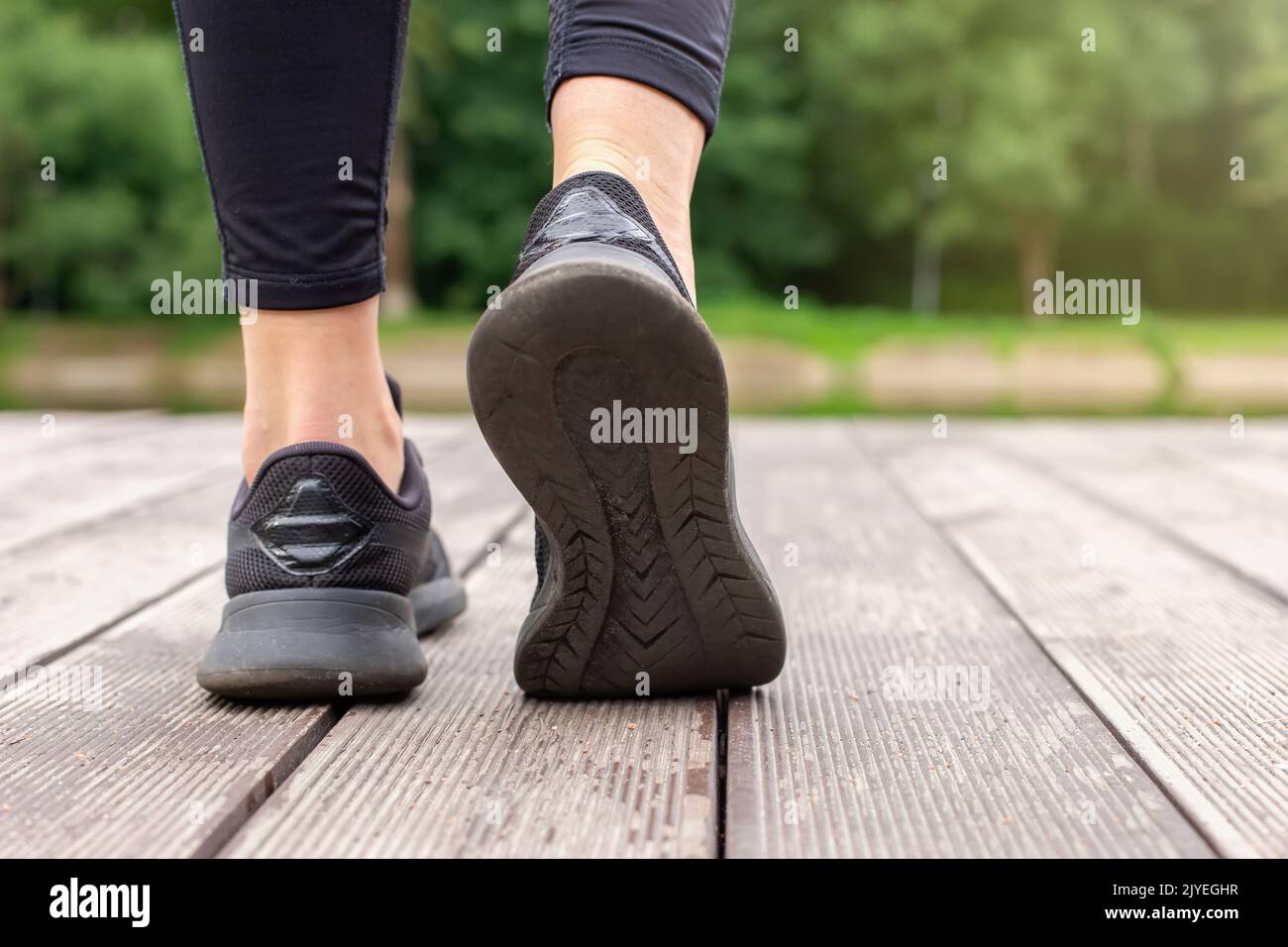 Primo piano delle gambe delle donne in sneaker nere che camminano su un ponte di legno Foto Stock