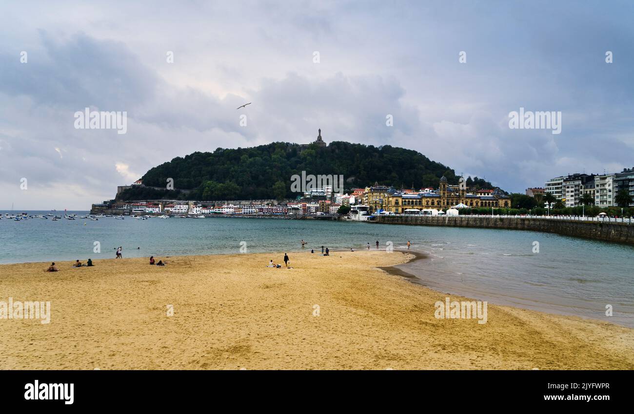 Paesaggio della spiaggia di la Concha nella città di San Sebastian, in una giornata di sole con la gente che si gode la spiaggia e il Monte Urgull sullo sfondo. Foto Stock