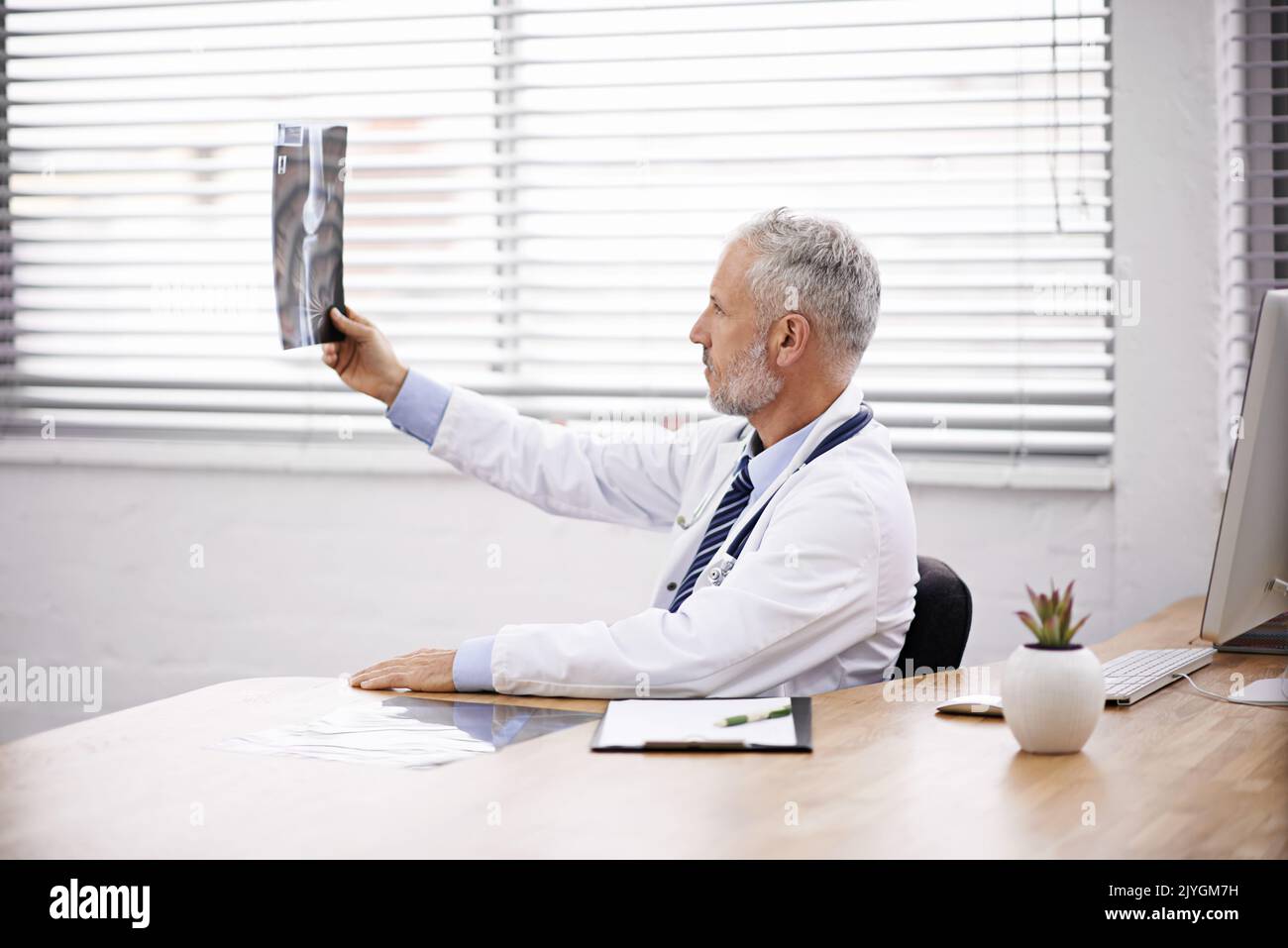 Identificare una diagnosi al problema medico. Un medico maschio maturo che analizza una radiografia nel suo ufficio. Foto Stock