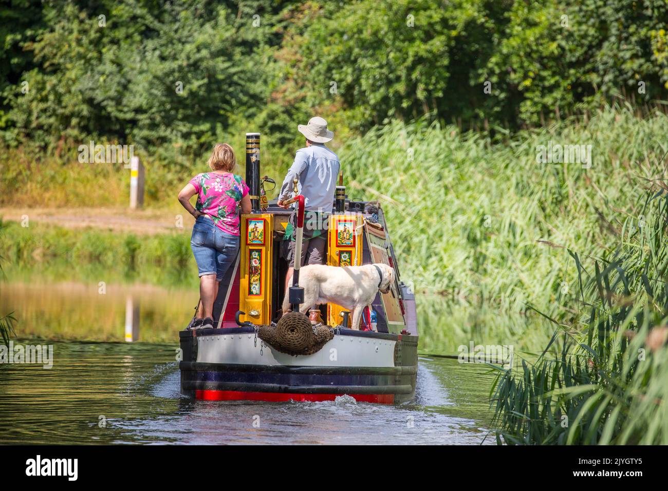 Vista posteriore di una coppia e del loro cane a bordo di una nave da crociera britannica che viaggia lungo un canale britannico in una giornata estiva di sole. Foto Stock