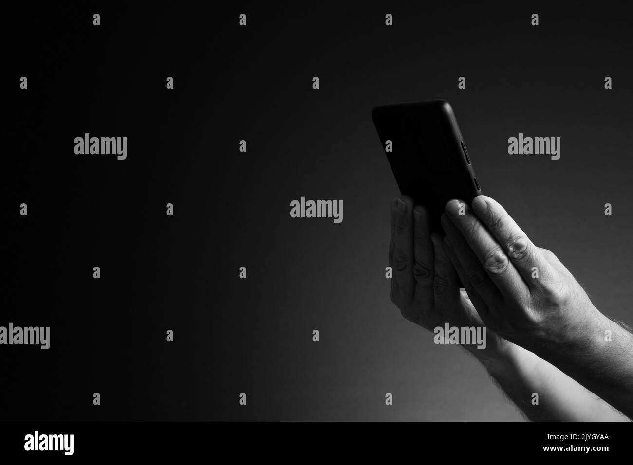 Immagine in bianco e nero, vista laterale delle mani dell'uomo che tiene lo smartphone isolato su sfondo scuro con spazio copia Foto Stock