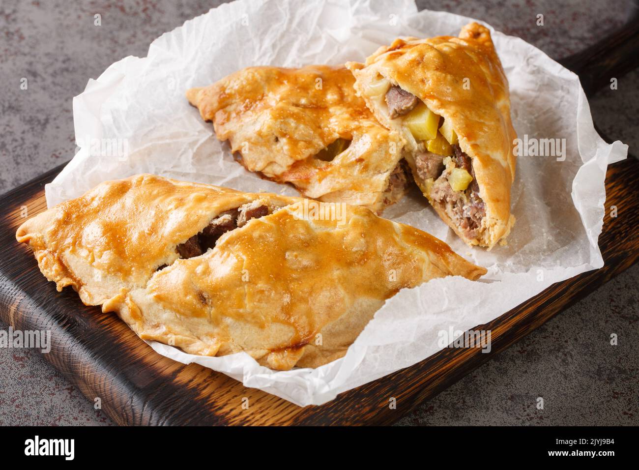 Torta al forno di pasty Cornish riempita con carne e patate primo piano sulla carta sul bordo di legno. Orizzontale Foto Stock