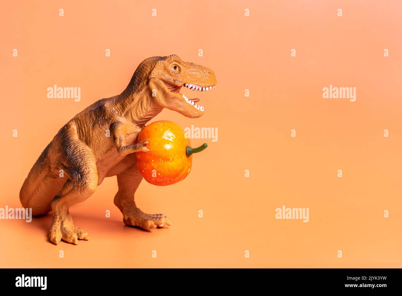 Giocattolo dinosauro Tyrannosaurus che tiene zucca nelle sue zampe isolato su sfondo arancione festivo auguri di festa giorno di Halloween felice, Ciao autunno creativo Foto Stock