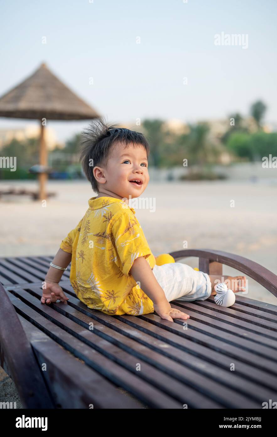 Bambino in vacanza sulla spiaggia seduto sul lettino al tramonto. Bambino maschio di un anno in vacanza al mare seduto sul lettino Foto Stock
