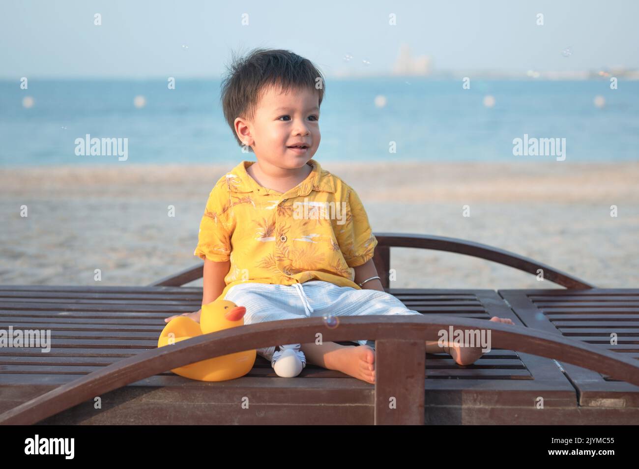 Bambino in vacanza sulla spiaggia seduto sul lettino circondato da bolle di sapone al tramonto. Un bambino maschio di un anno in vacanza presso la sittina sul mare Foto Stock