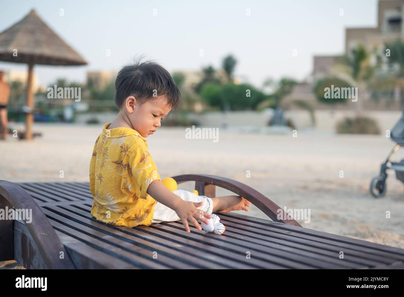 Bambino in vacanza sulla spiaggia seduto sul lettino al tramonto. Bambino maschio di un anno in vacanza al mare seduto sul lettino Foto Stock