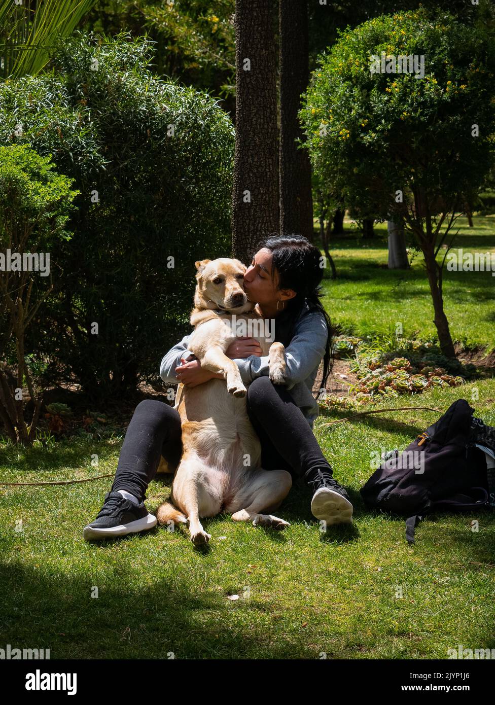 Donna peruviana seduta sul prato, abbracciando un cane giallo Mongrel e circondato da un sacco di natura Foto Stock