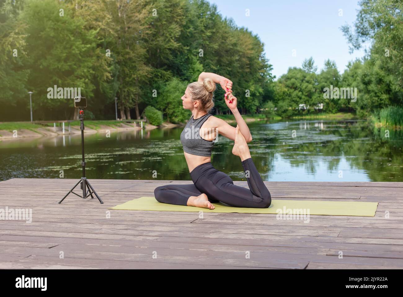 Una bella donna in una piattaforma di legno in estate, fa yoga in stagno nel parco Foto Stock