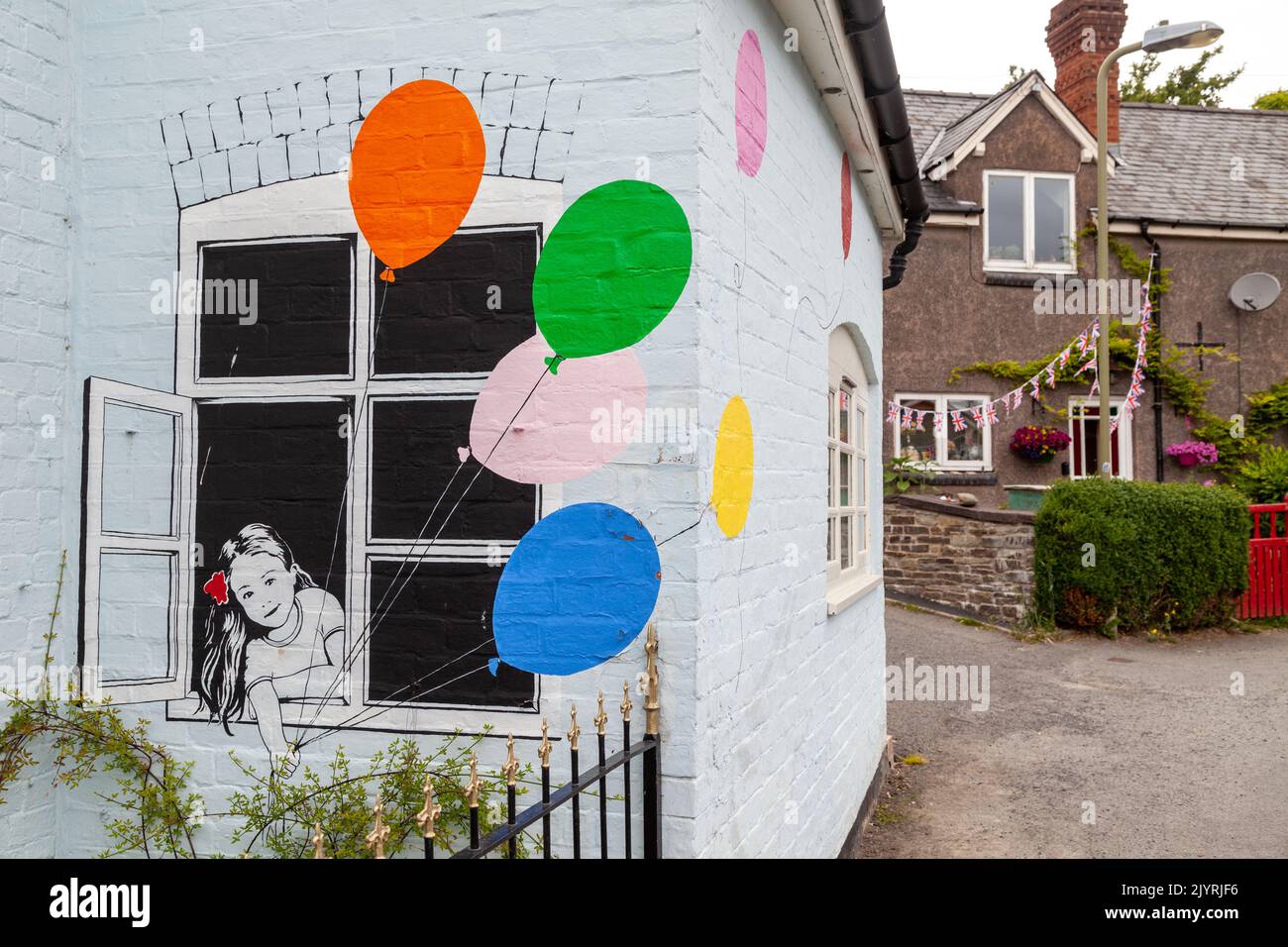 Arte graffiti in stile banksy di una ragazza con palloncini che si affaccia da una finestra su una casa nel castello episcopale. Foto Stock