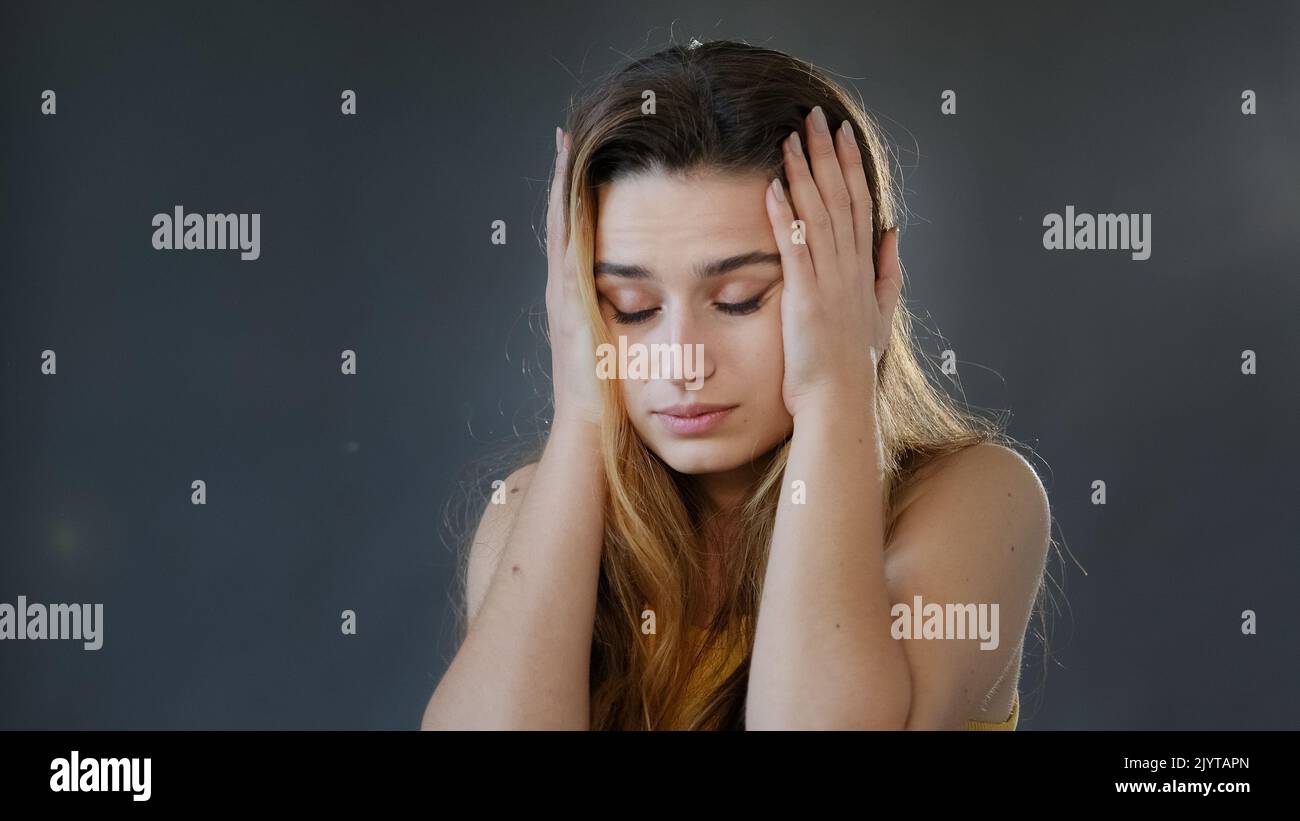 Ritratto femminile su sfondo grigio in studio giovane ragazza pensiva donna donna donna modello guardando la fotocamera si distende mani a lato sconosciuto tenendo la testa da Foto Stock