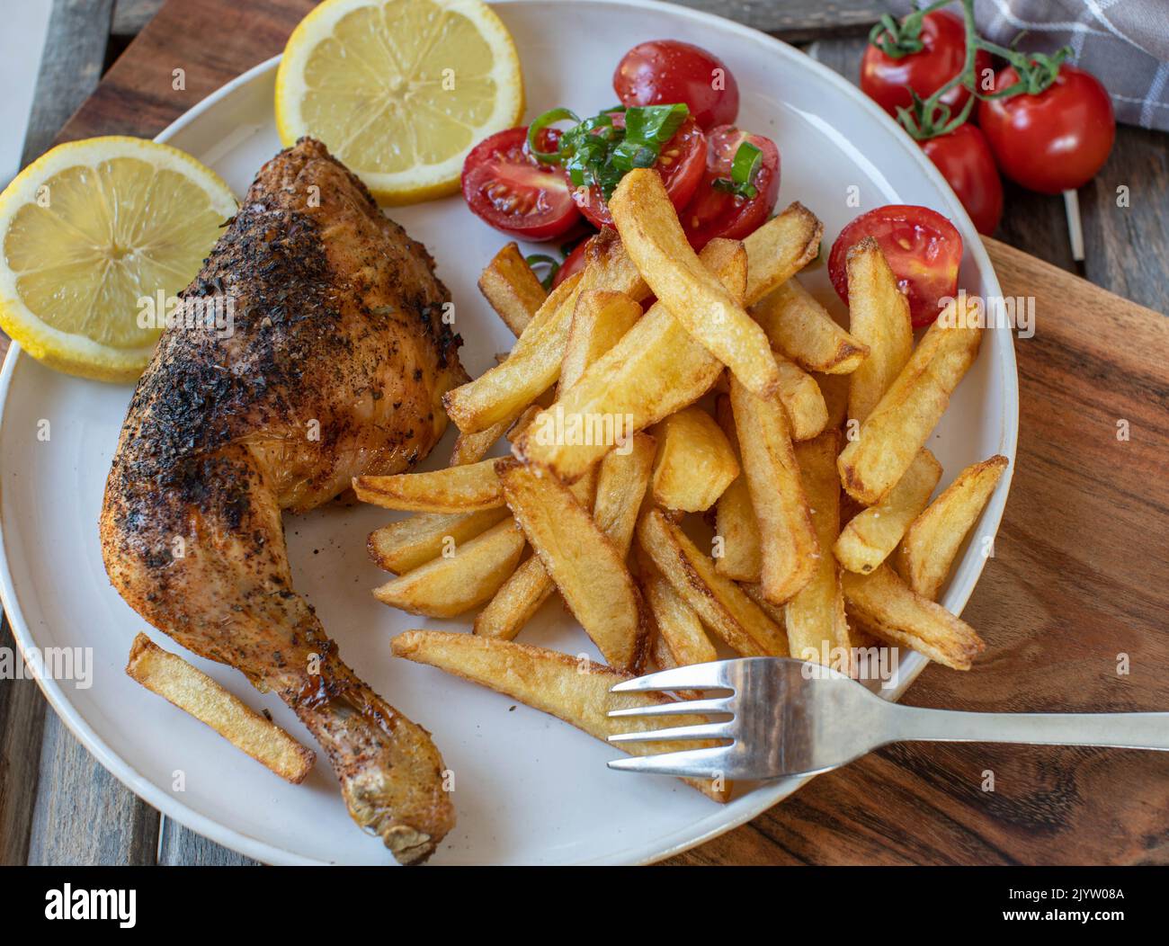 Coscia di pollo croccante con patatine fritte fatte in casa e insalata di pomodoro Foto Stock