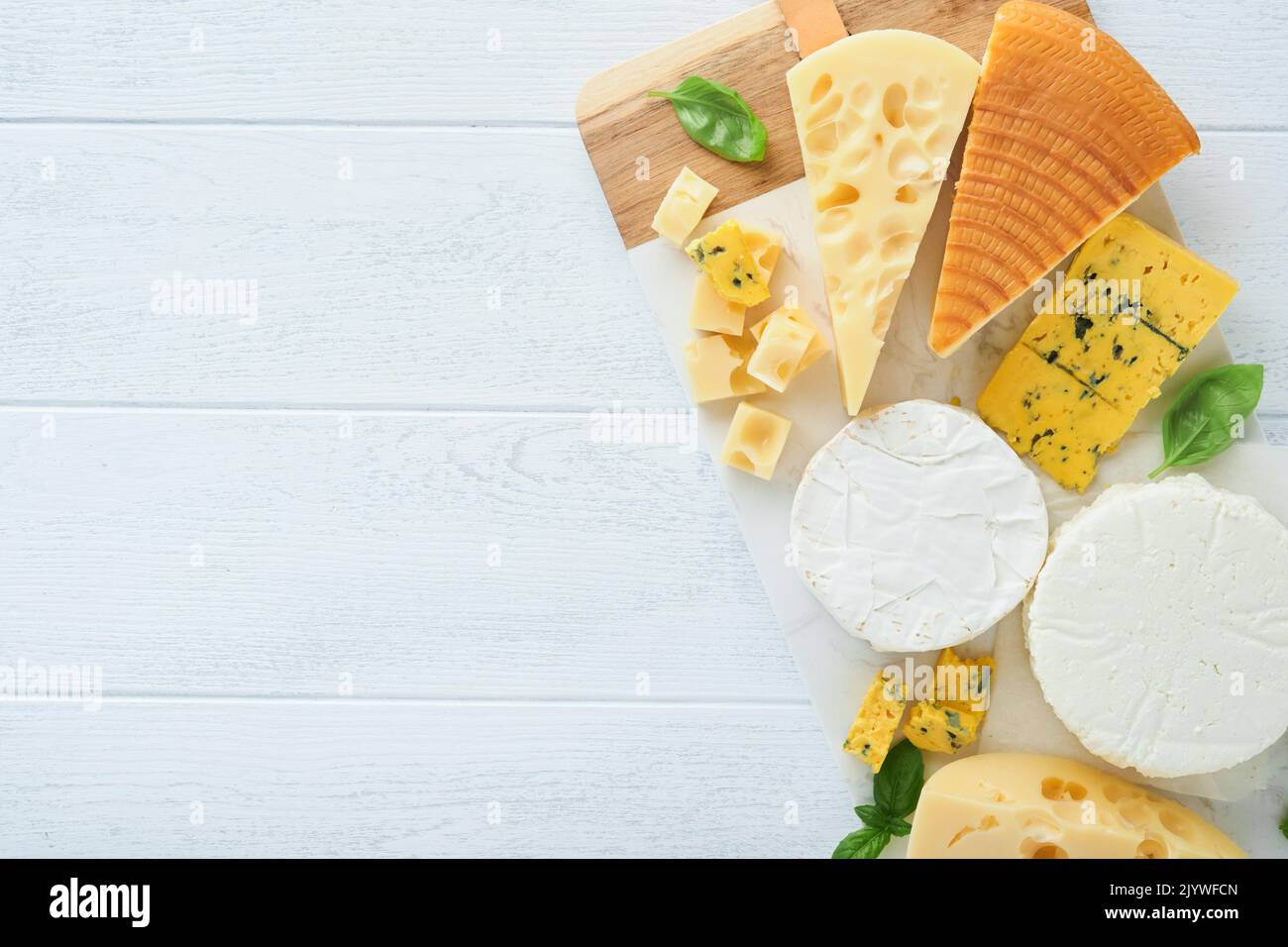 Formaggi assortiti o assortiti. Maasdam, formaggio affumicato, camembert, formaggio blu, parmigiano, brie formaggio con basilico e pepe su tavola di marmo bianco Foto Stock