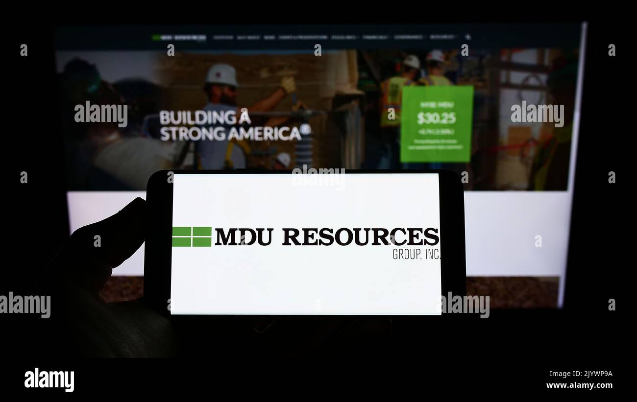 Persona che detiene uno smartphone con il logo della società statunitense MDU Resources Group Inc. Sullo schermo davanti al sito Web. Messa a fuoco sul display del telefono. Foto Stock