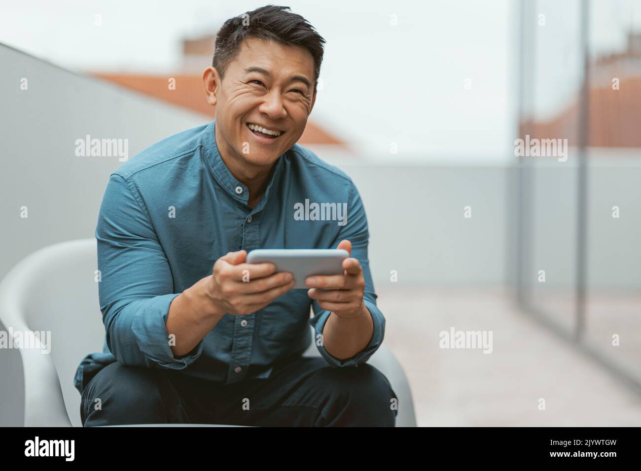 Sorridente uomo d'affari asiatico che usa il telefono durante la pausa Foto Stock