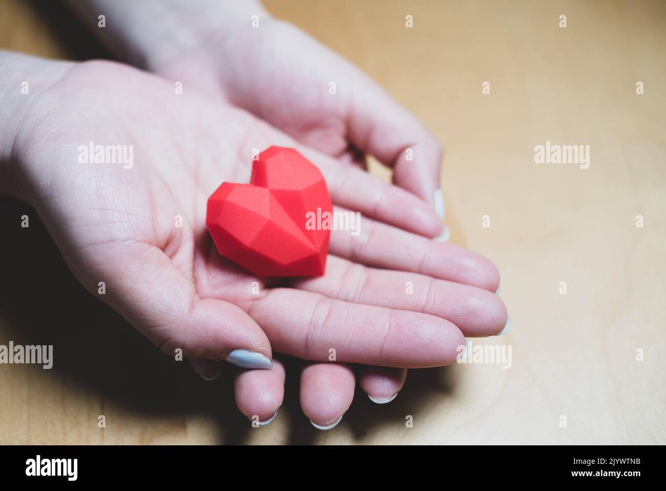 Adulto che tiene il cuore rosso nelle mani sopra un tavolo di legno. Relazioni familiari, assistenza sanitaria, concetto di cardiologia, concetto di salute del cuore Foto Stock