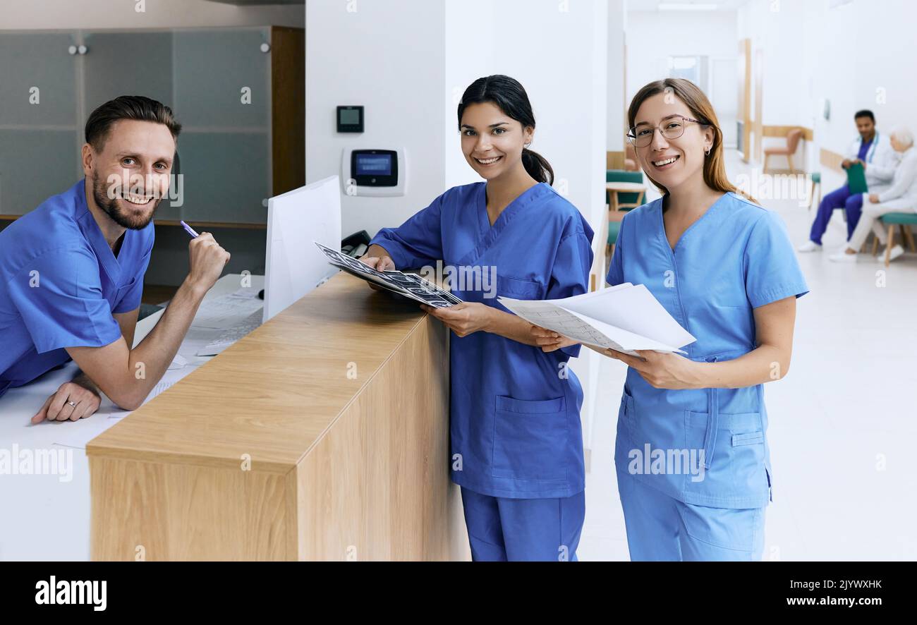 Infermiera in servizio che parla con gli assistenti medici durante la giornata lavorativa in una clinica medica in piedi vicino al banco della reception nella hall dell'ospedale. personale medico del cl Foto Stock