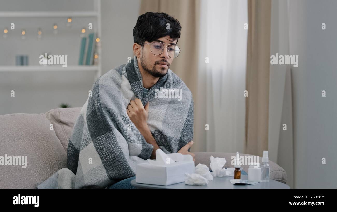 Giovane uomo arabo malato ragazzo con gli occhiali si siede a casa divano coperto con coperta plaid soffre di malattia fredda stagionale allergia virus che soffia runny Foto Stock